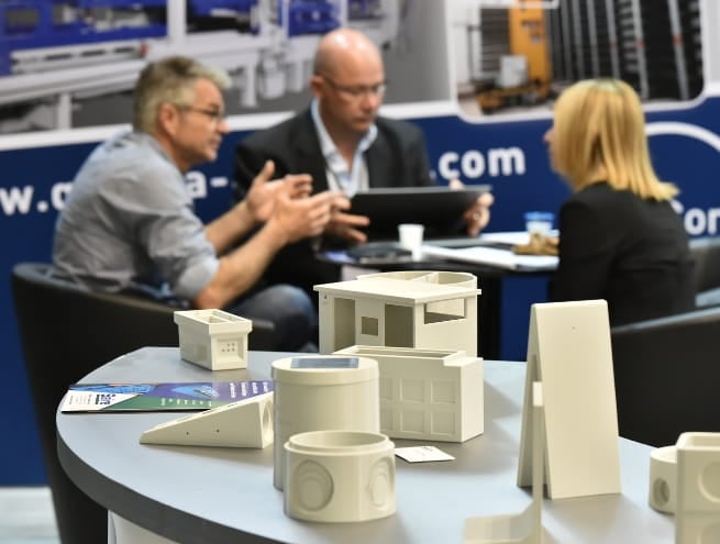 photo of construction models on a table with 3 people talking in the background